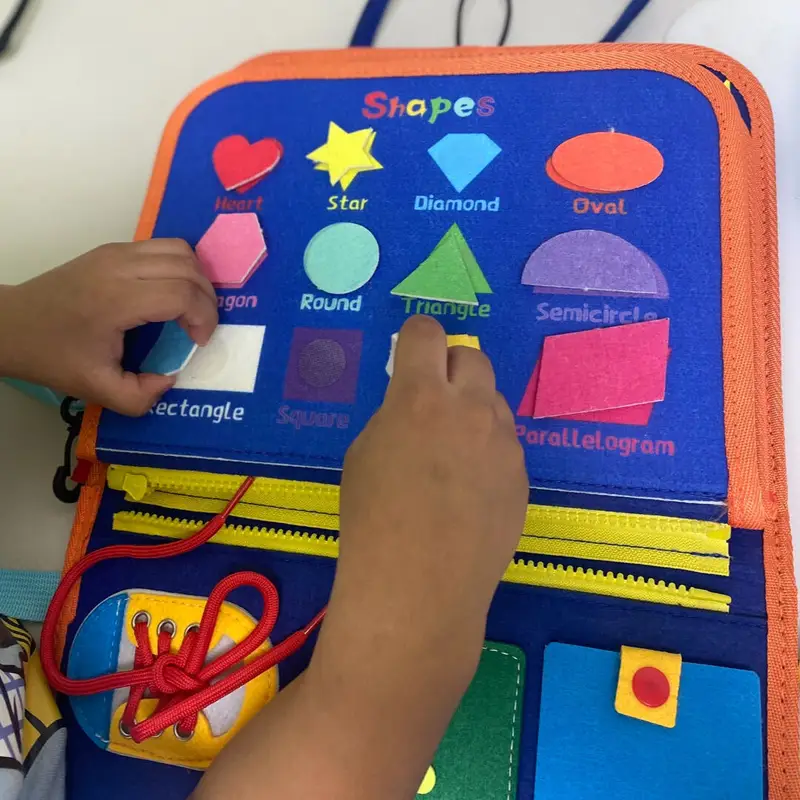 A child&rsquo;s hands pressing felt shapes onto a colorful busy board with zippers and a lace-up shoe