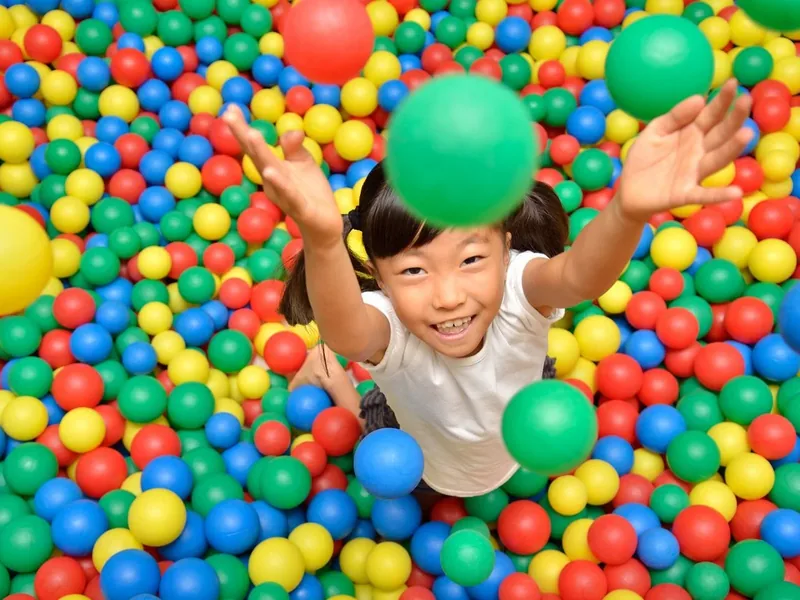 A young girl reaching up and playing in a colorful ball pit
