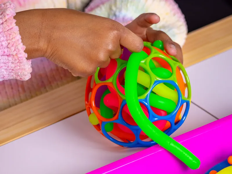 A child's hand gripping a colorful textured sensory ball toy