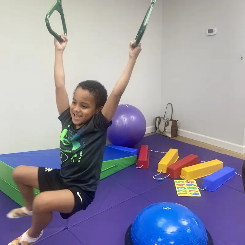 A laughing boy swinging from gymnastic rings over the mats in the sensory gym