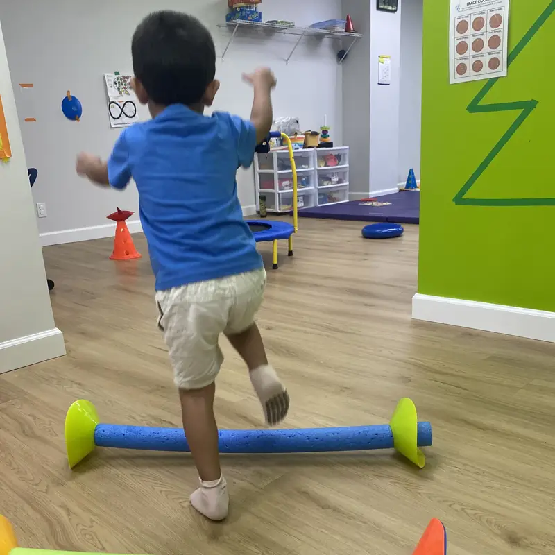 A boy stepping over a foam-noodle hurdle on an obstacle course in the sensory gym