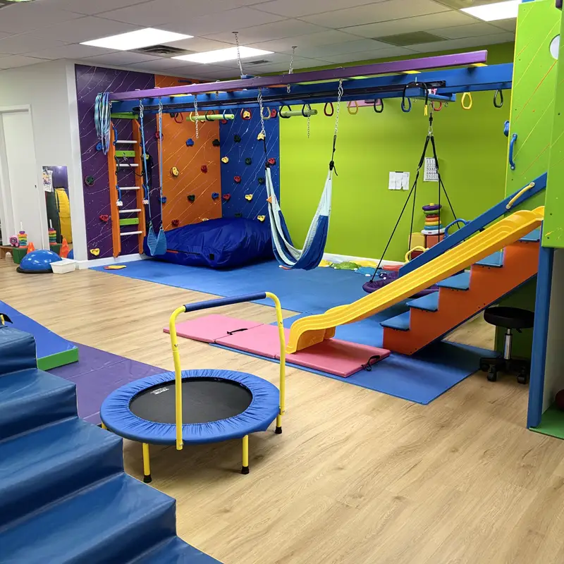 The Planet Sensory gym: a climbing wall, monkey bars, a hammock swing, a slide and a mini trampoline on colorful mats
